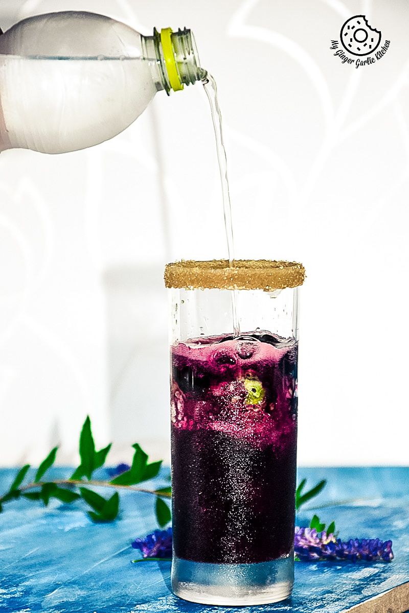 someone pouring water into a glass of blueberry kiwi cooler