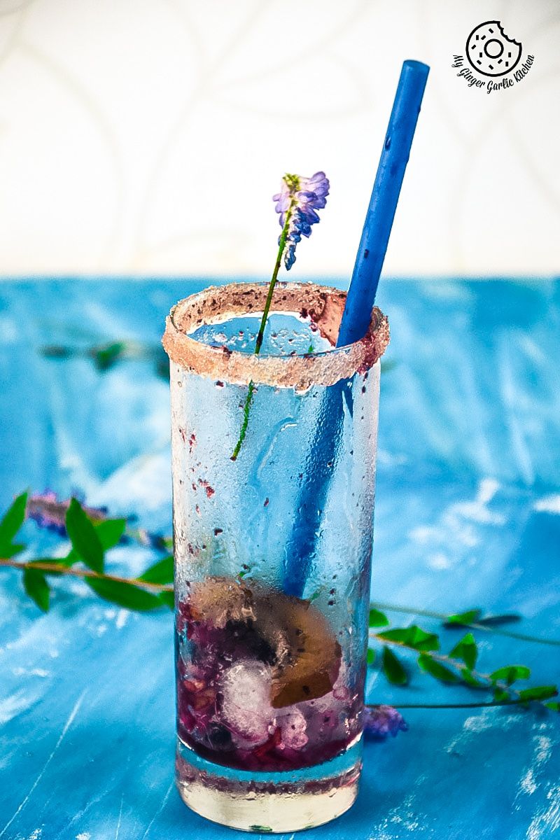 an empty blueberry kiwi cooler glass with a blue straw and a flower in it