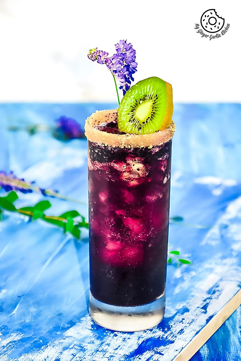 a glass of blueberry kiwi cooler with a kiwi on the rim and a flower on the rim