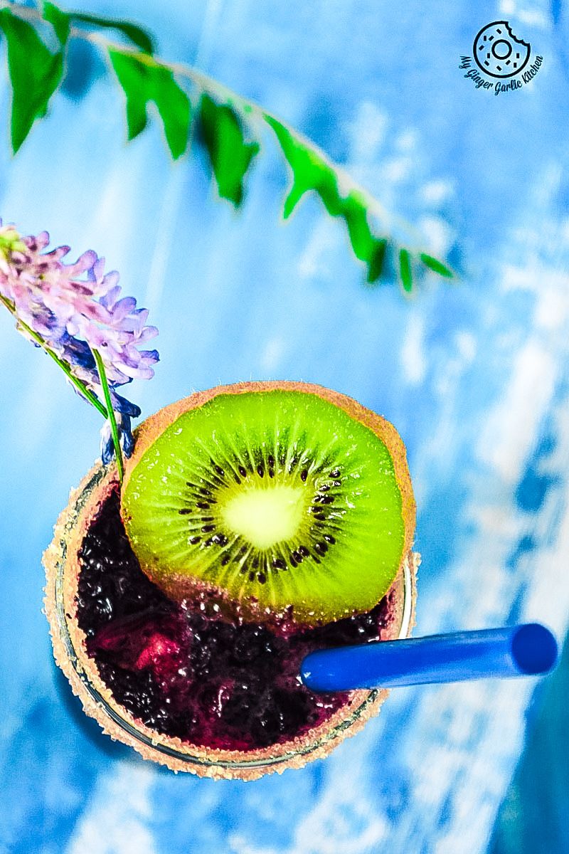 a blueberry kiwi cooler with a kiwi slice and a blue straw