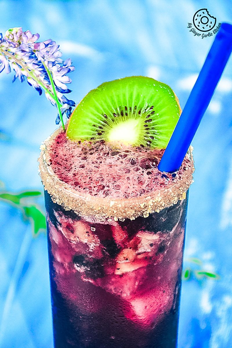 a blueberry kiwi cooler with a kiwi on the rim and a blue straw