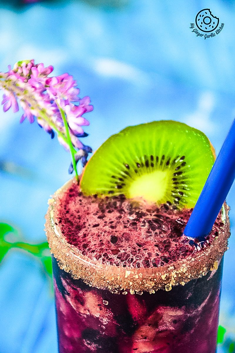a blueberry kiwi cooler drink with a kiwi on the rim and a blue straw