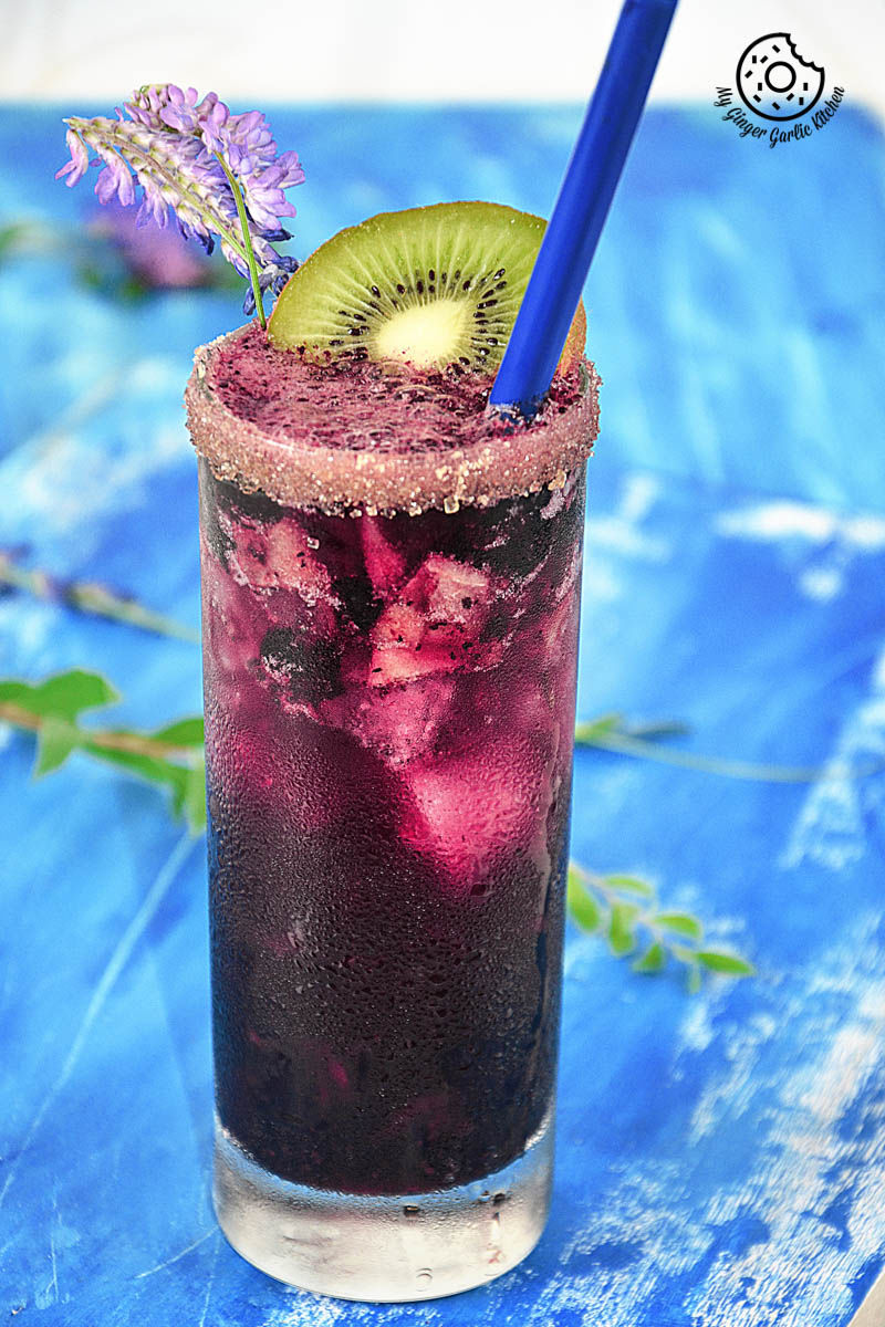 a blueberry kiwi cooler with a blue straw and a kiwi on the rim