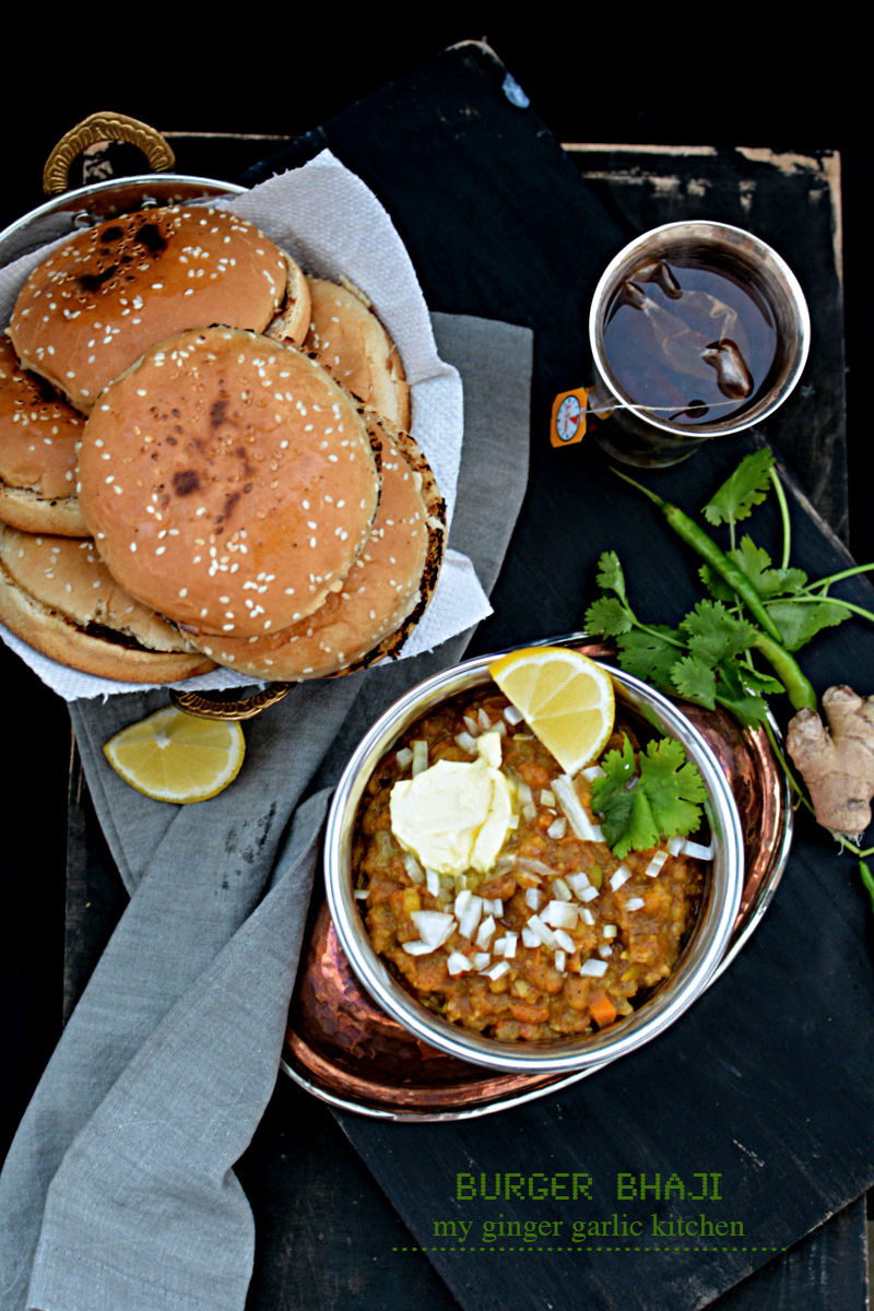 a bowl of bhaji on a tray with a burger and a cup of tea