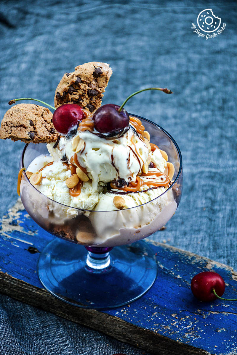 a ice cream sundae in a glass with caramel chocolate chip cookies salted peanuts a cherry on top