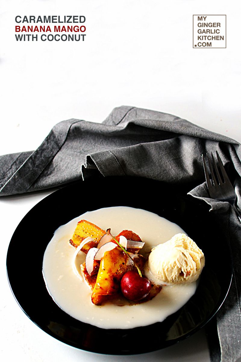 a black plate of caramelized banana mango with coconut with ice cream and cherry on it