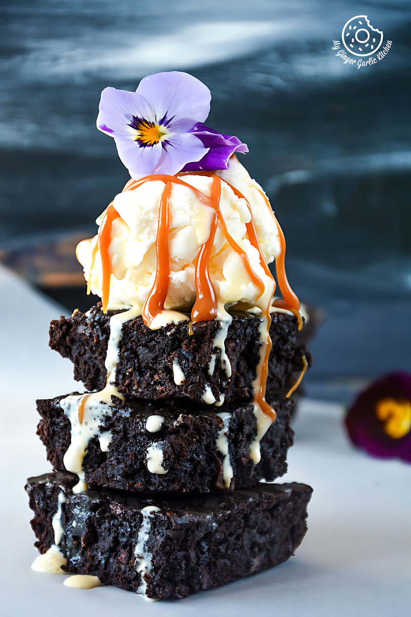 a stack of carrot brownies with ice cream, caramel sauce and a flower on top