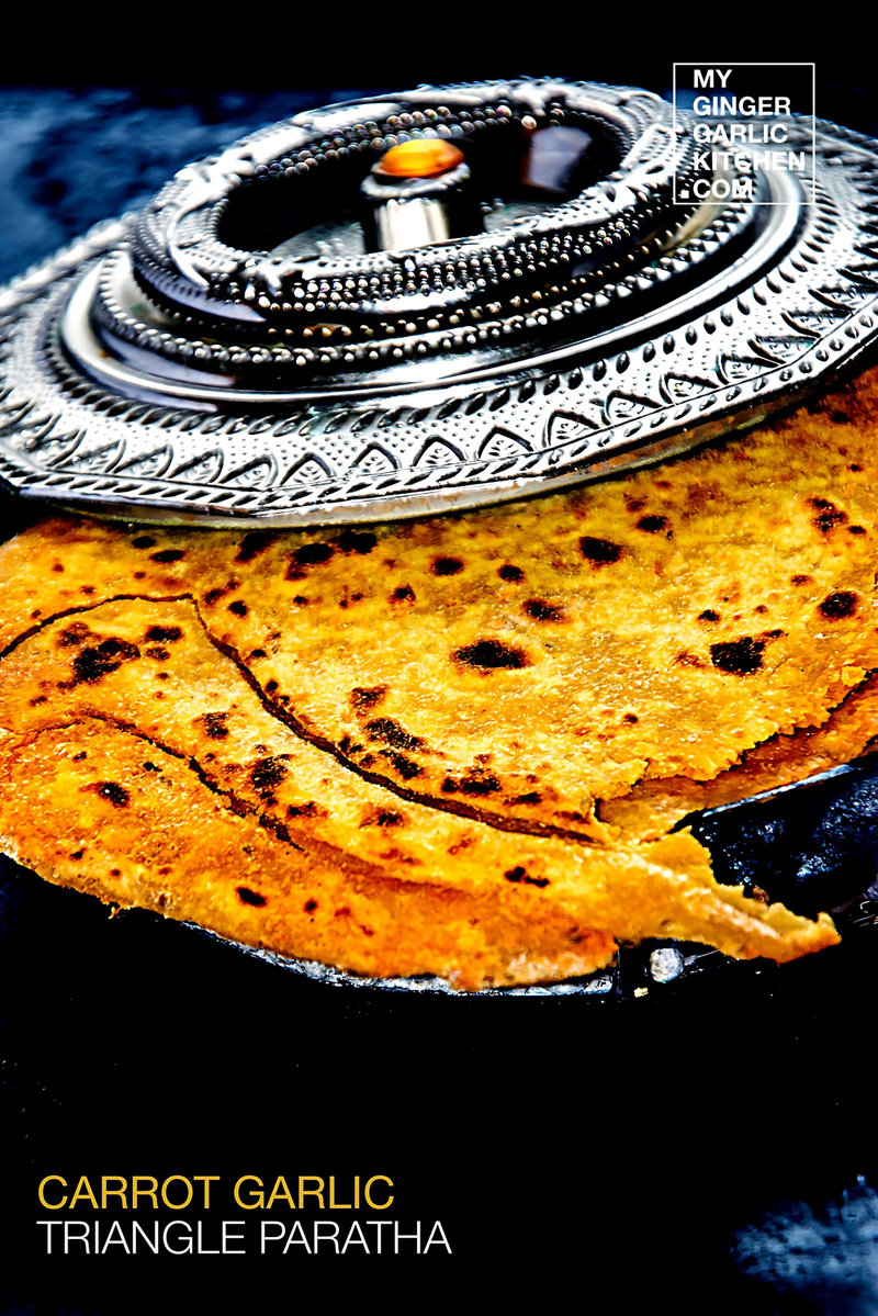 a plate with a carrot garlic triangle paratha on a silver plate