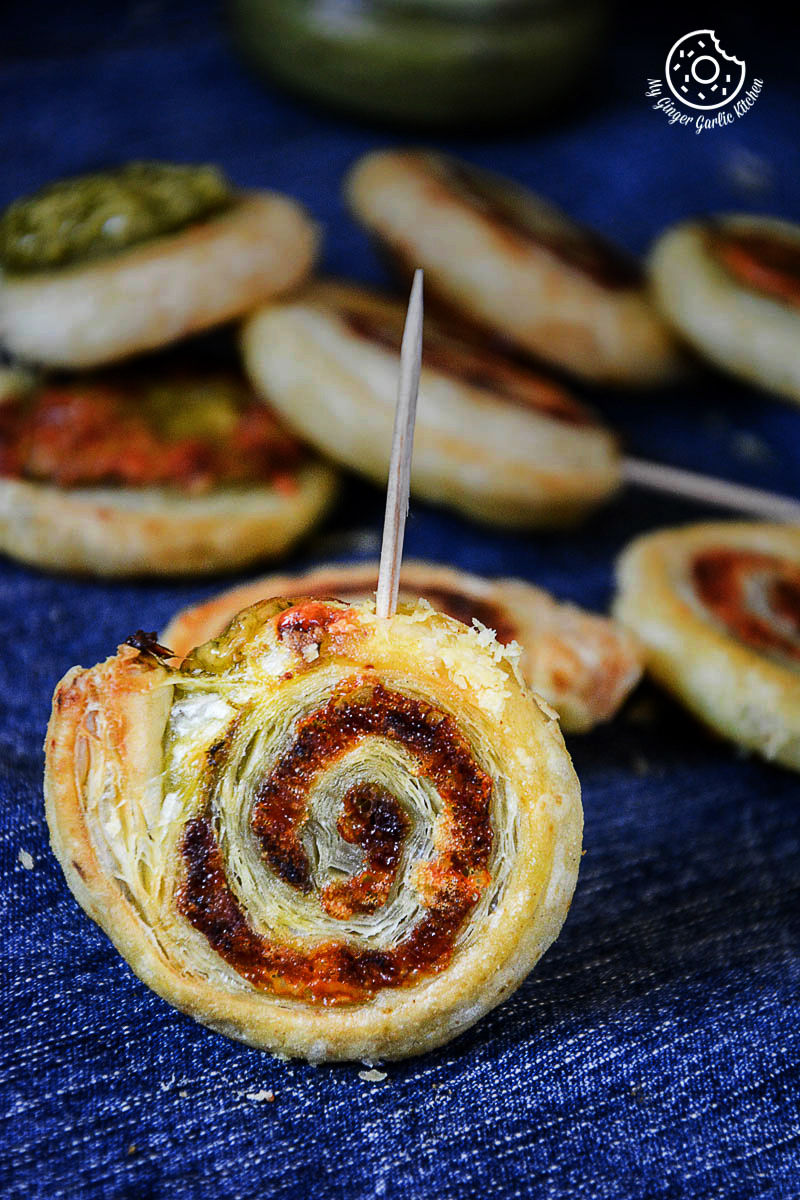several small cheesy garlicky pesto puffa pastry swirls with a toothpick sticking out of them
