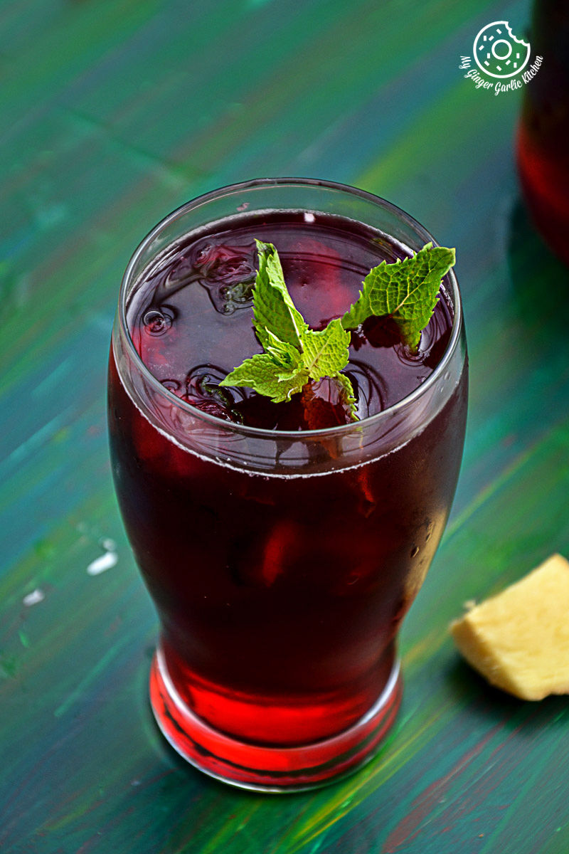 a glass of cherry iced tea with lemon with mint leaves on the rim