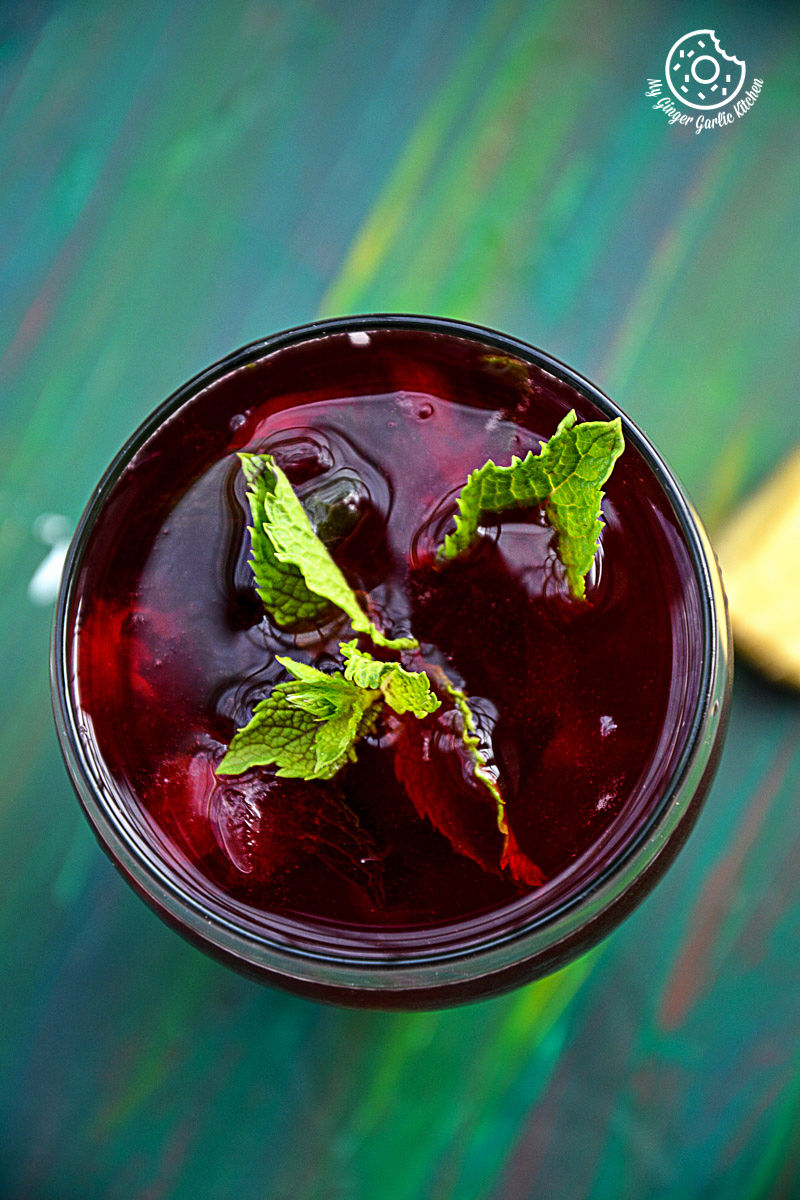 a glass of cherry iced tea with ice cubes and mint leaves