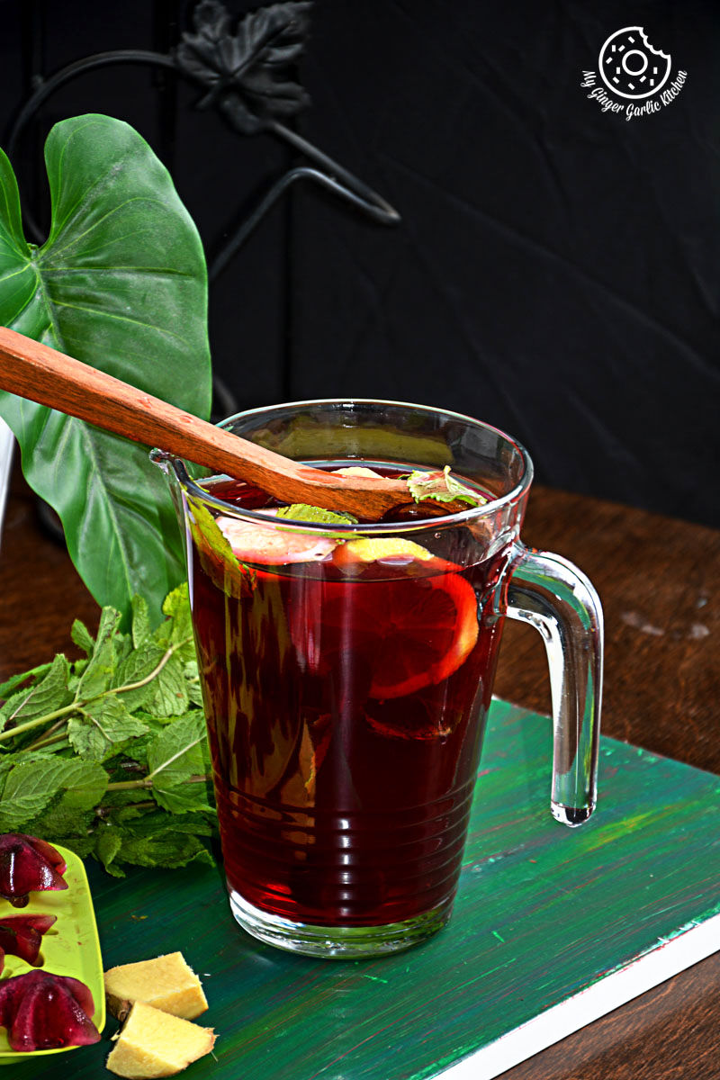 a pitcher of cherry iced tea with lemon mint ginger and honey with a wooden spoon on a table