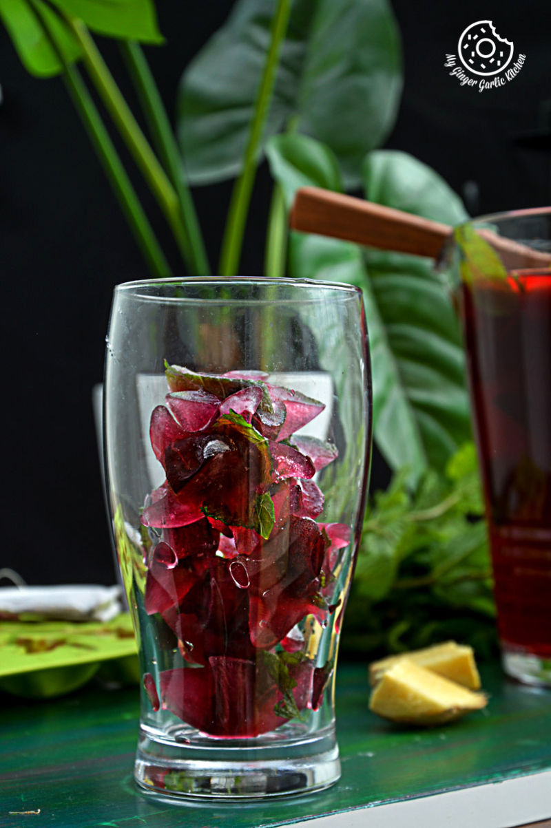 a glass with a bunch of red cherry iced tea ice cubes and a plant in background