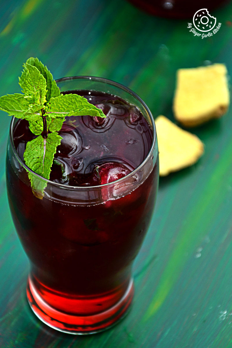 a glass of cherry iced tea with lemon mint ginger and honey with a mint leaf on top
