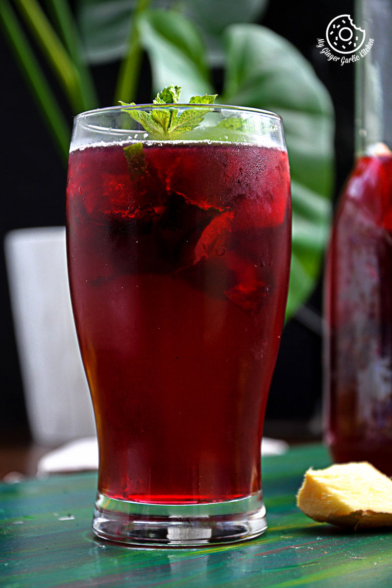a glass of cherry iced tea with lemon mint ginger and honey with a mint leaf on top