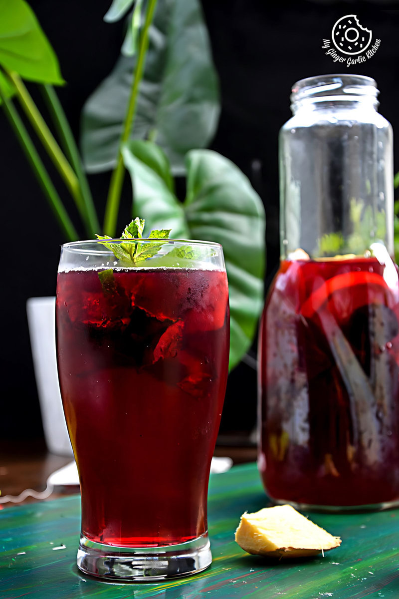 a glass of cherry iced tea with lemon with a ginger slice on the side and a bottle in background
