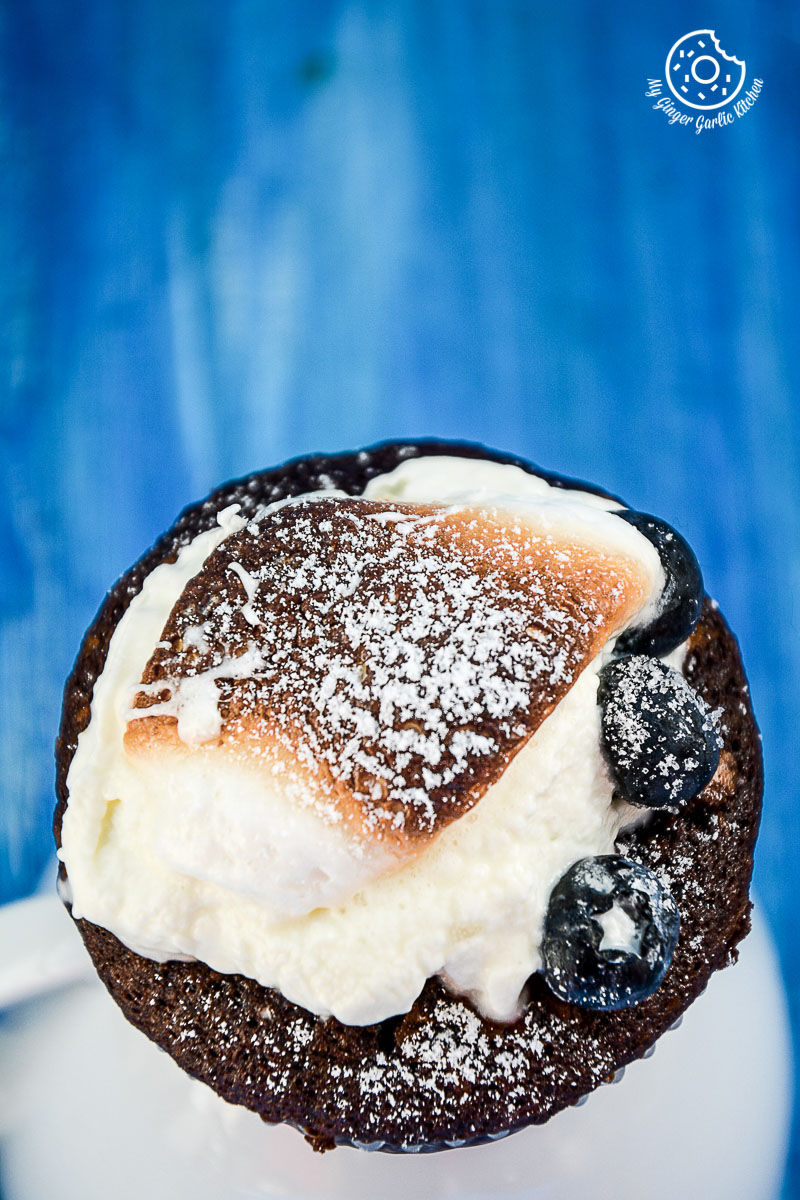 a chocolate cream cheese muffin with blueberries with a frosting and powdered sugar on top