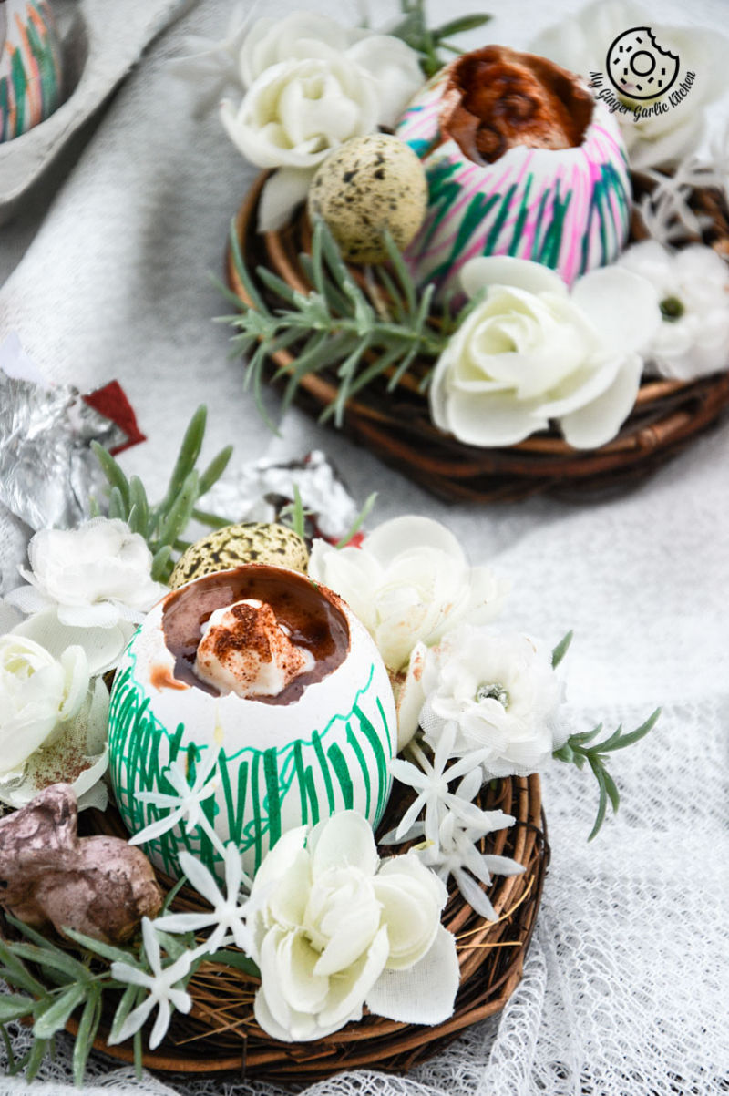 there are two baskets with two chocolate lassi egg cups and flowers on a table