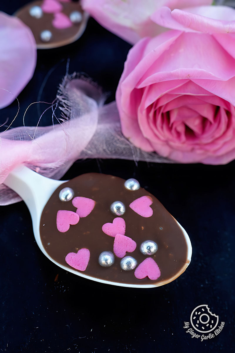 a chocolate spoon with pink hearts on it with a rose in background