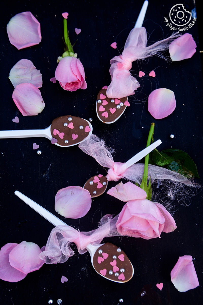a chocolate spoons with pink hearts on them with pink roses on a black surface