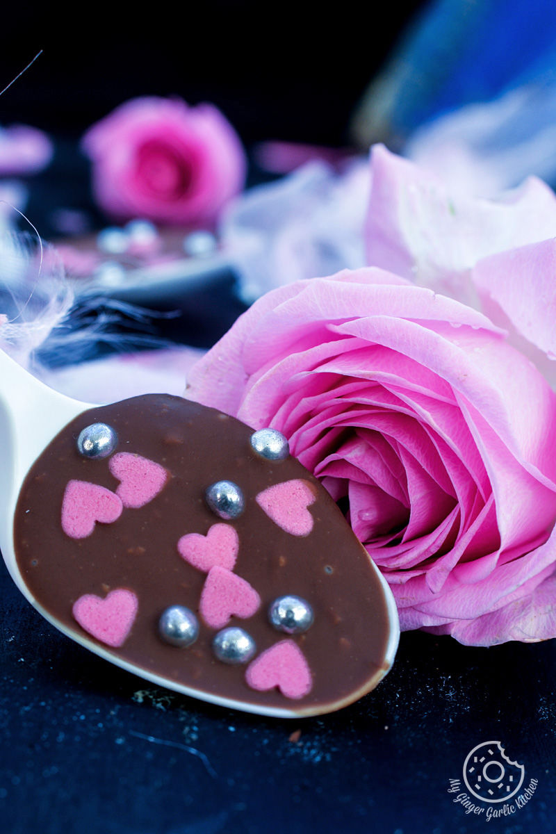 a chocolate spoon with pink hearts on it with a rose in background