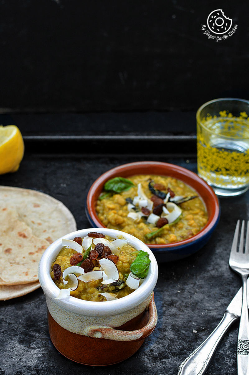 two bowls of cholar dal with some roti flatbread and a glass on a tray