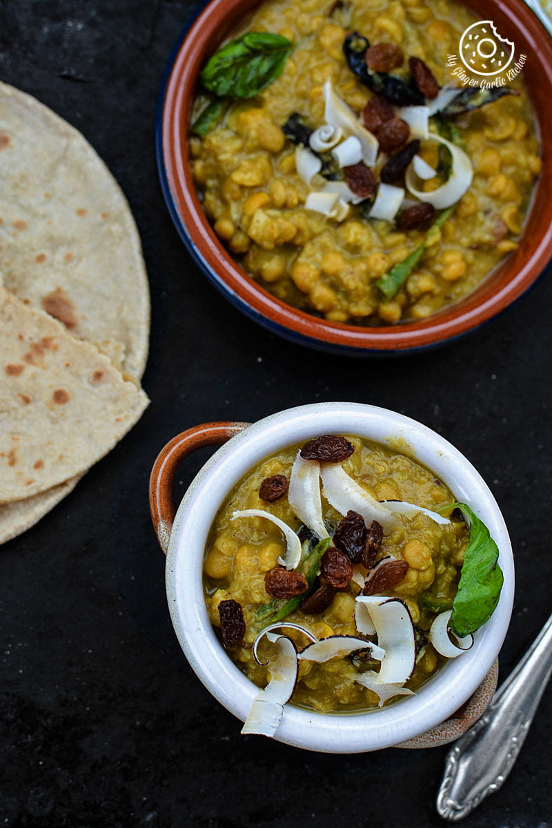two bowls of cholar dal with some roti flatbread and a cutlery on a tray
