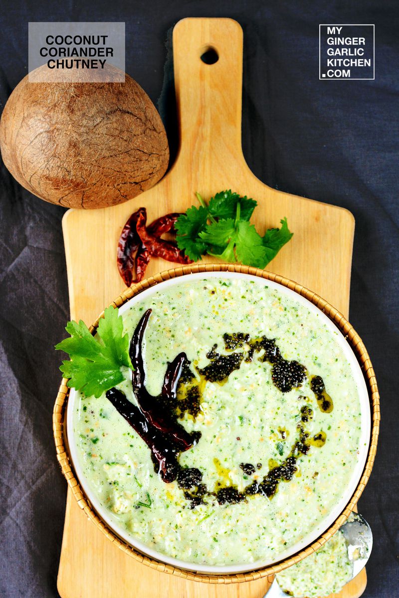 a bowl of coconut coriander chutney with a coconut and dried red chilies on a cutting board