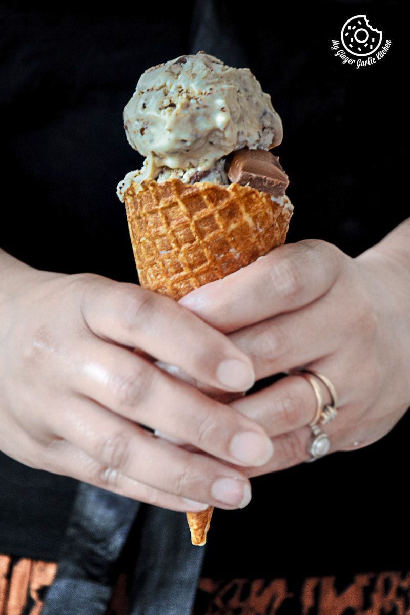 someone holding a cone of creamy coconut coffee chocolate chunk ice cream with chocolate