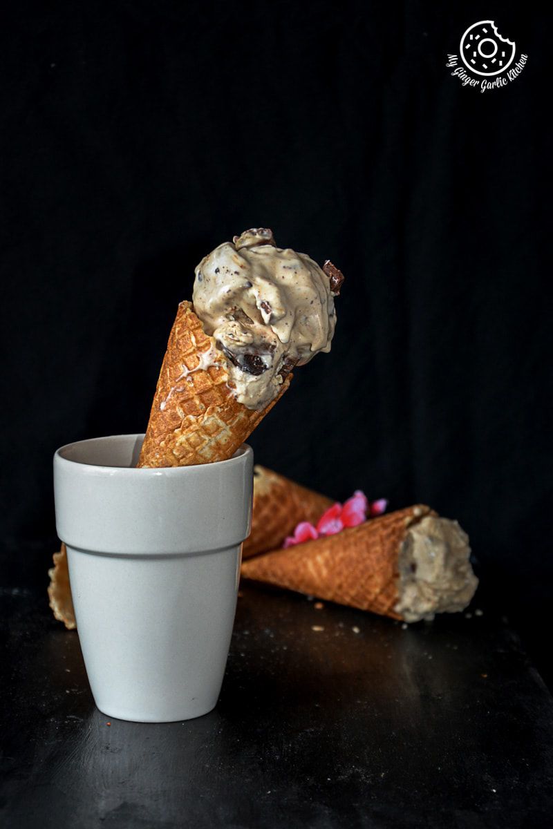 a cone of creamy coconut coffee chocolate chunk ice cream in a cup with some more cones in background