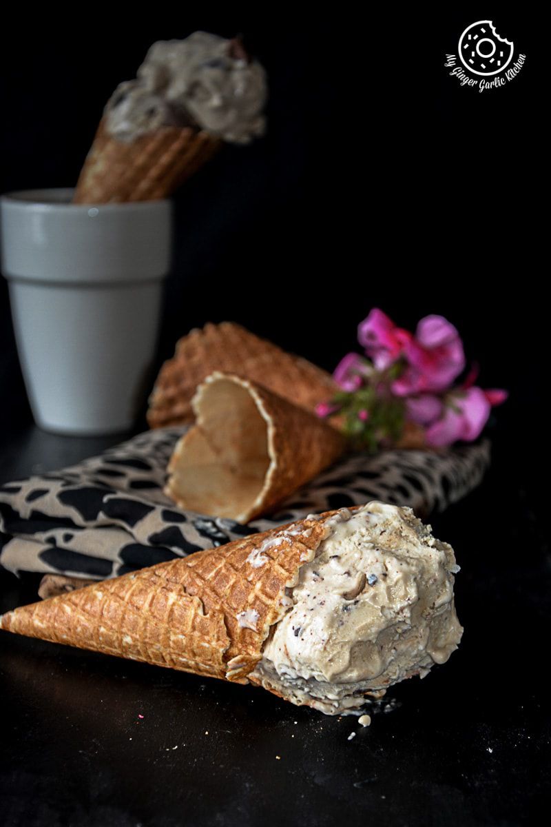 a scoop of creamy coconut coffee chocolate chunk ice cream in a cone on a table