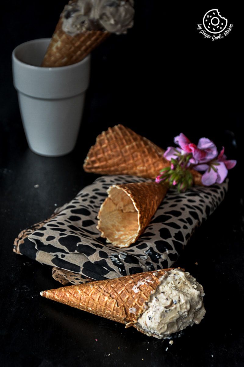 a waffle cone with a scoop of creamy coconut coffee chocolate chunk ice cream on it with two more cones in background