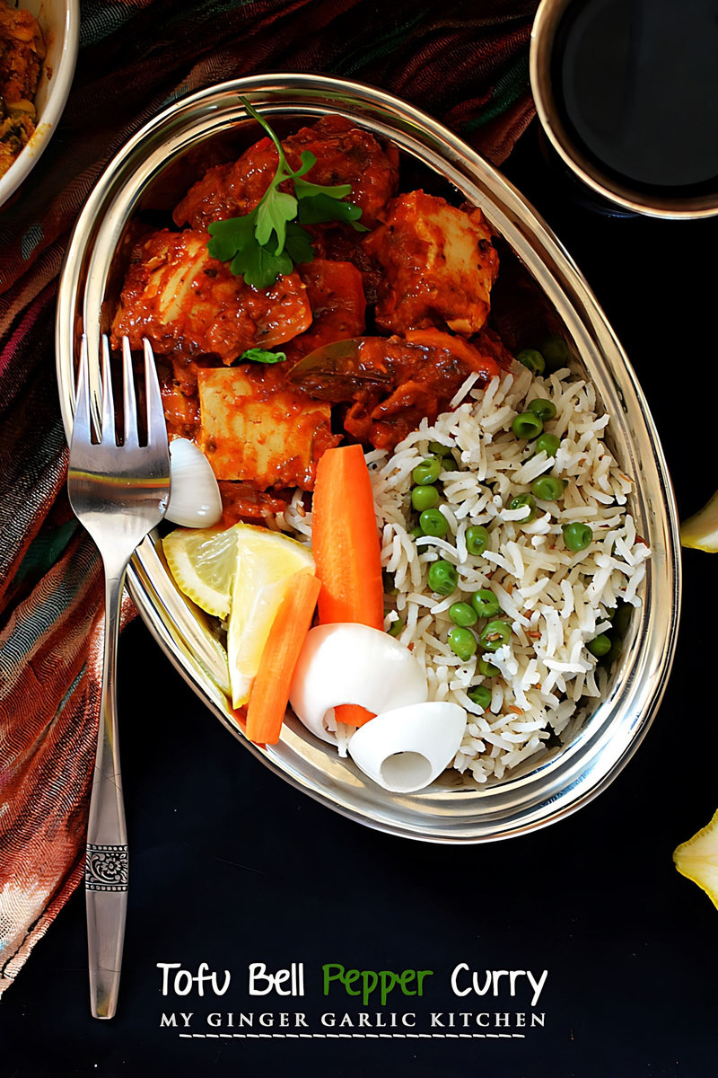 a plate of creamy tofu bell pepper curry with rice, carrots, and lemon