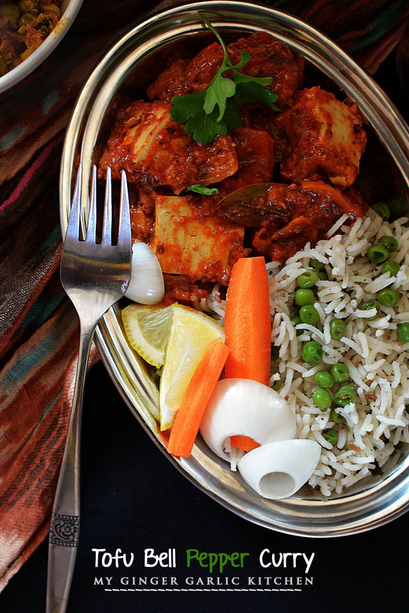 a plate of creamy tofu bell pepper curry with pulao, carrots, and onions