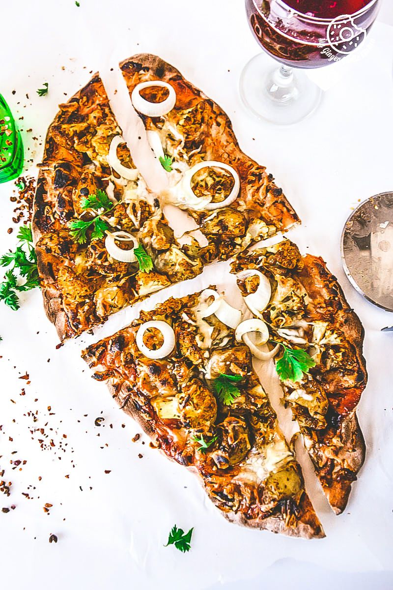 a curried cauliflower topped naan pizza with onions and cheese on it on a table