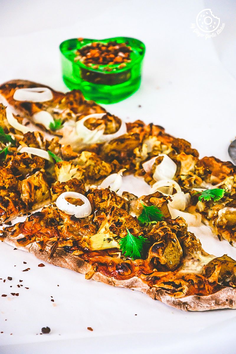 a curried cauliflower topped naan pizza with onions and other toppings on a plate