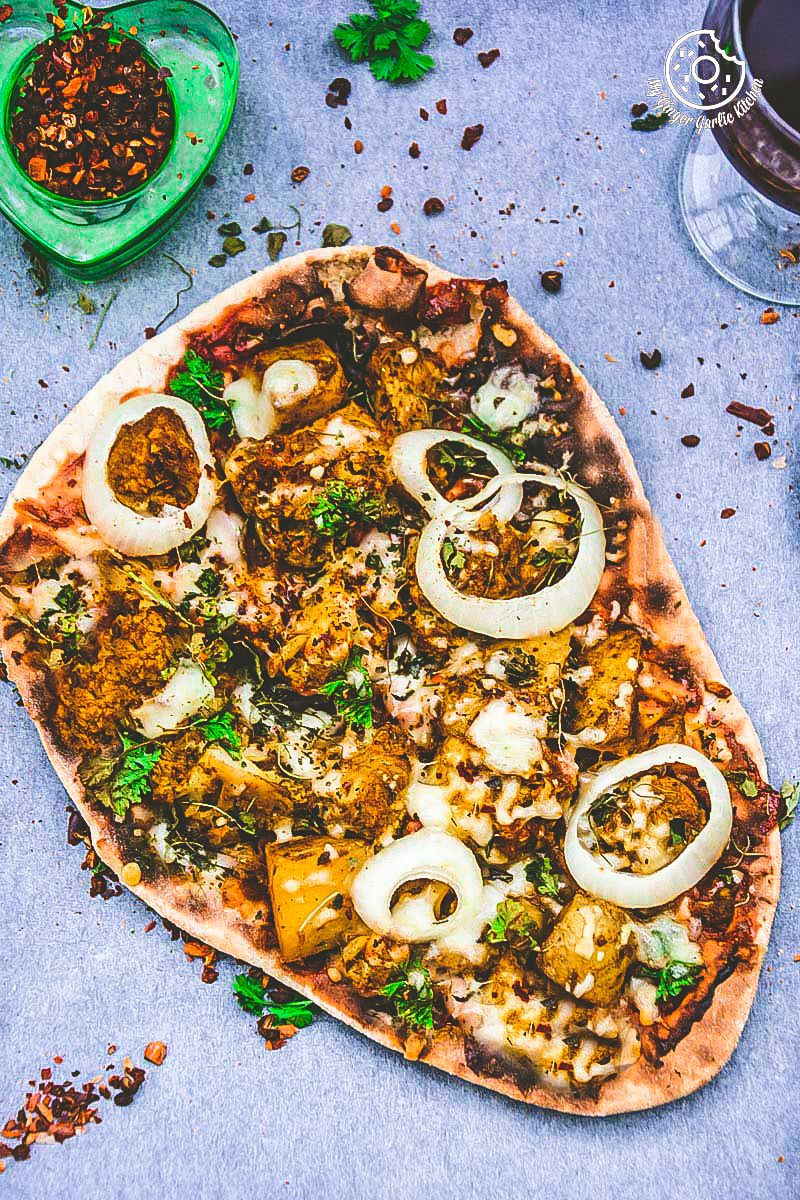 curried cauliflower topped naan pizza with onions and other toppings on a table