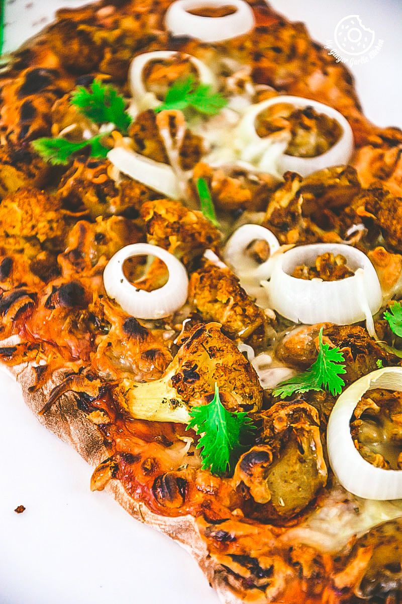 a curried cauliflower topped naan pizza with onions and mushrooms on it on a plate