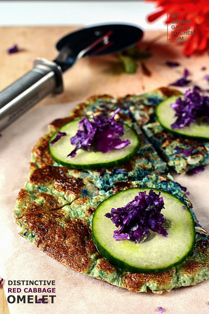 three pieces of red cabbage omelet tipped with cucumber slices and grated cabbage on a cutting board