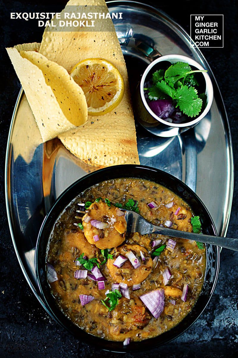 there is a bowl of rajasthani dal dhokli  with a spoon and some roasted papad and onions