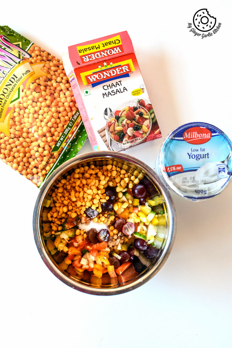 a bowl of fruity veggie boondi raita with other ingredients on a white table 