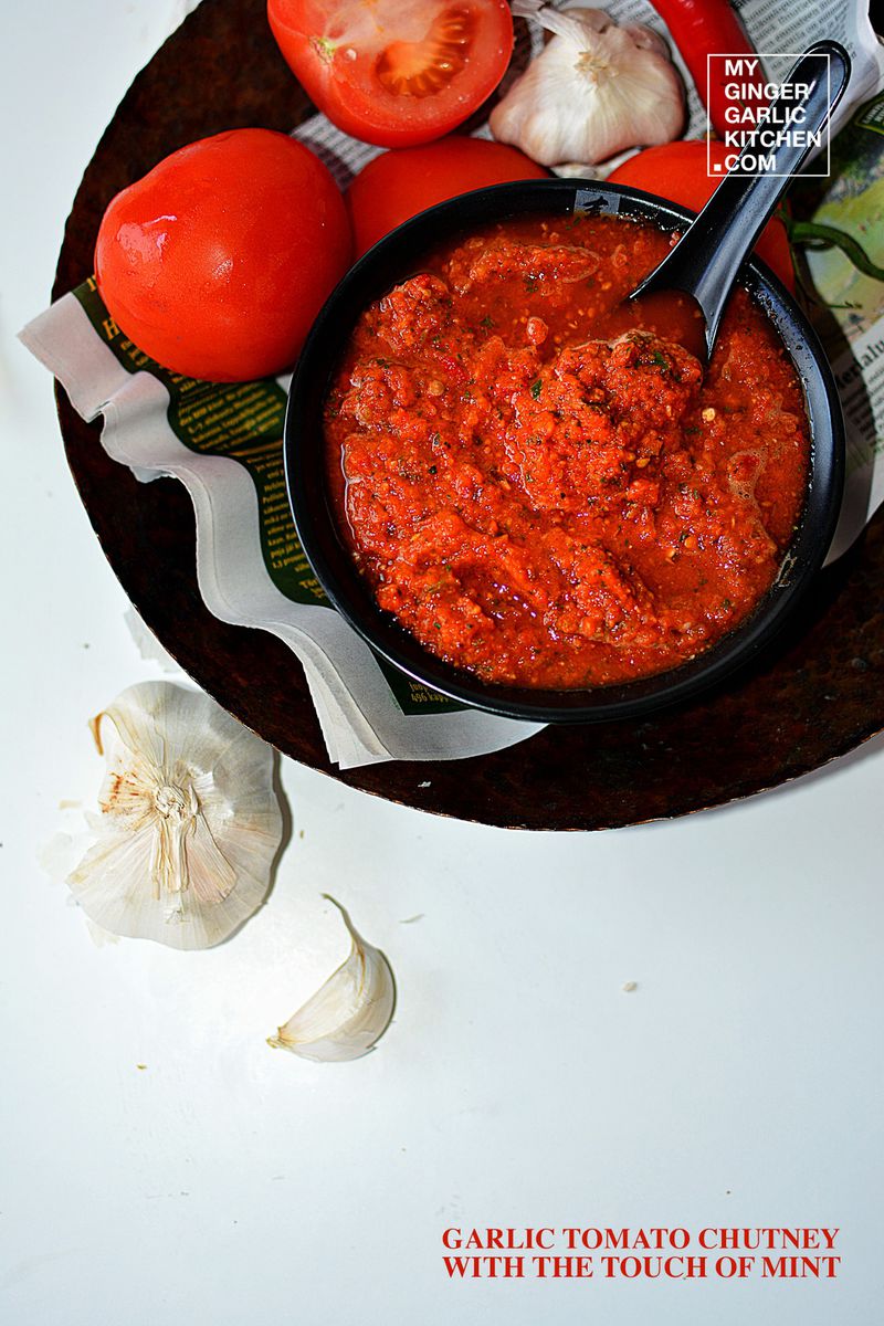 tomatoes, garlic, and garlic with a bowl of garlic tomato chutney on a plate