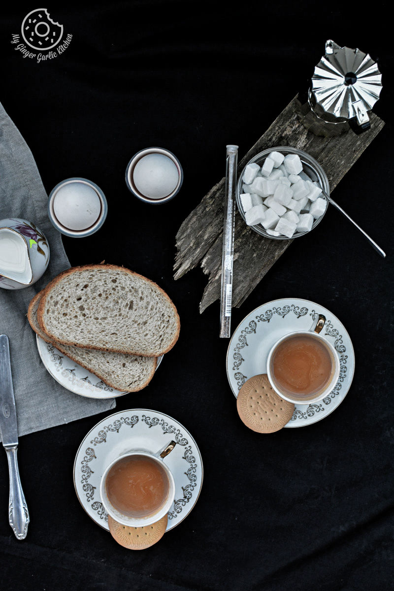 a table with a plate of bread with two cups of ginger cardamom tea on a saucer