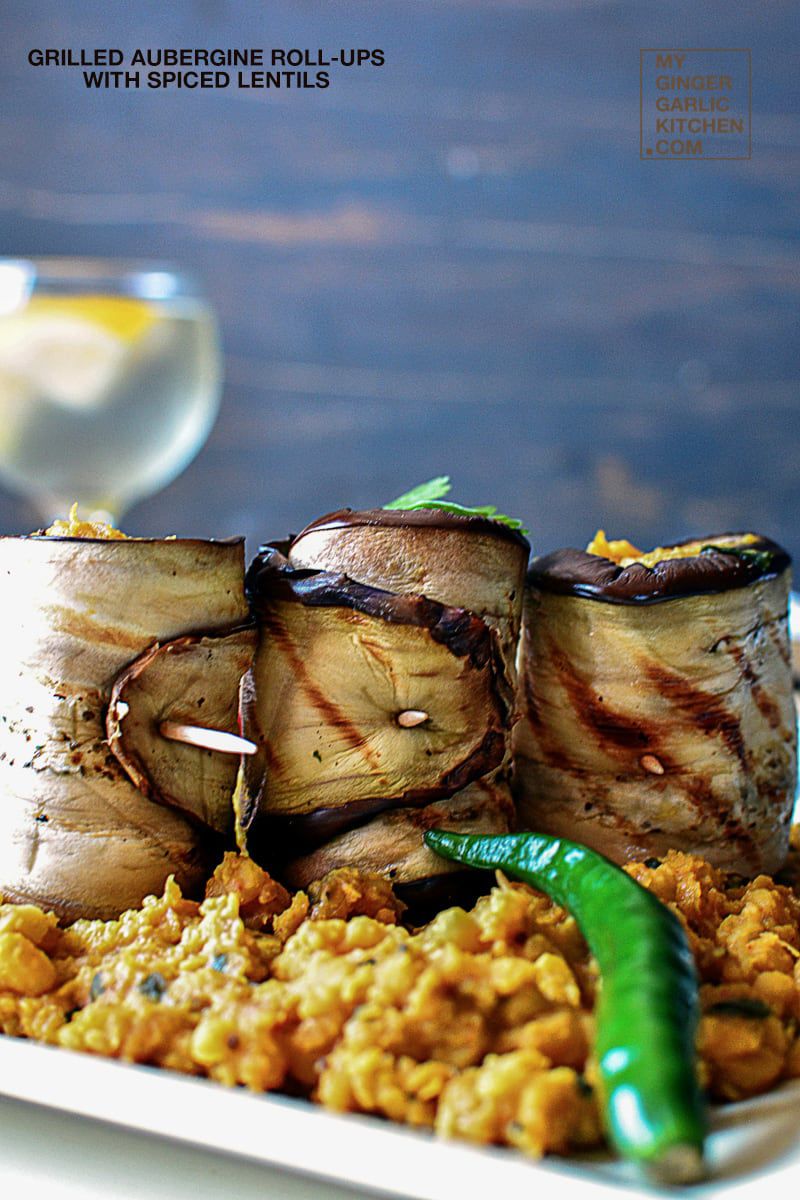 a plate of grilled aubergine roll ups on curried lentils with a glass of water