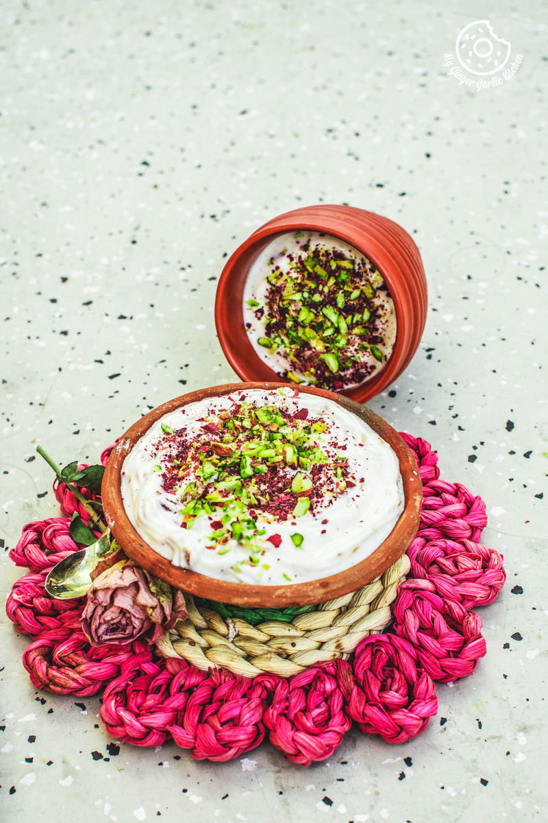 a bowl of rose shrikhand with a spoon rest on a pink mat with one more shrikhand bowl in background