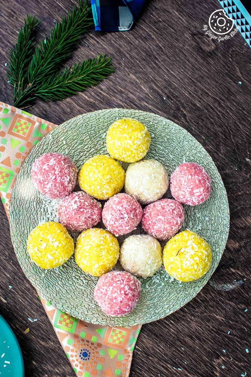 a plate with rose coconut ladoo, saffron coconut laddo, and coconut ladoo on a table