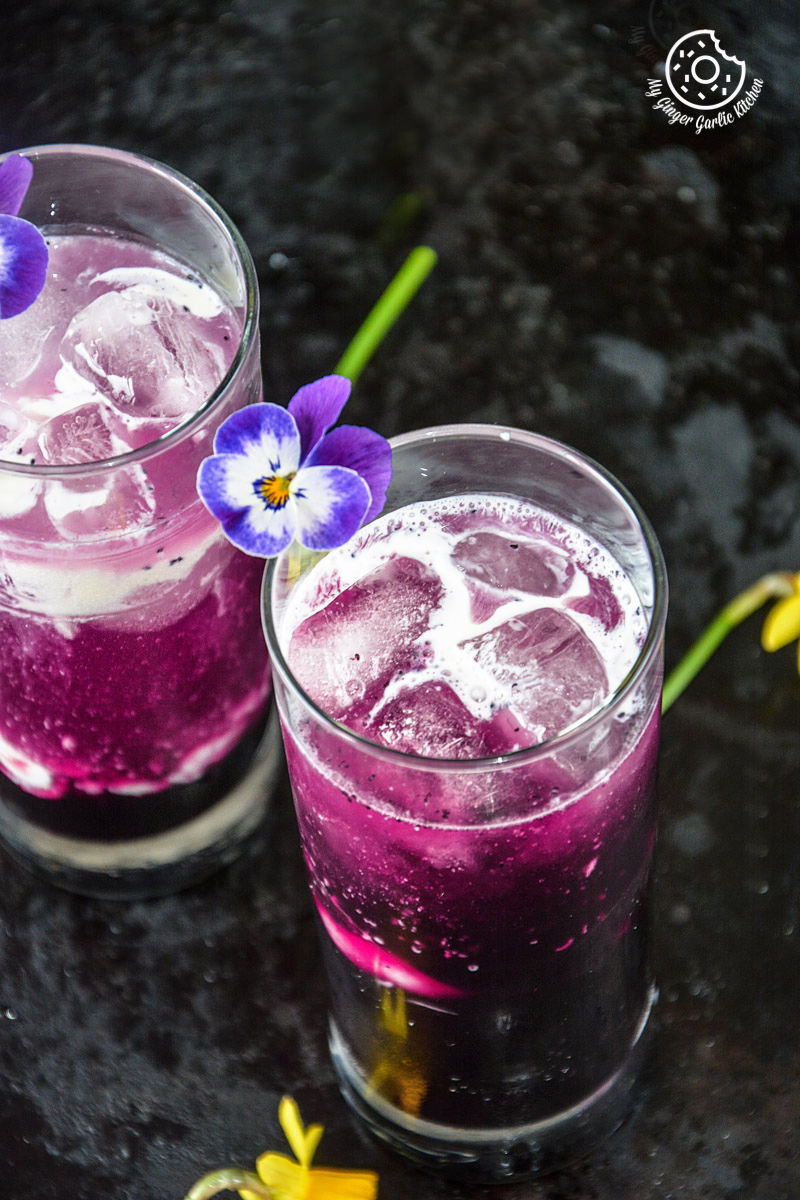 purple italian cream soda drink with ice and flower in glass on table