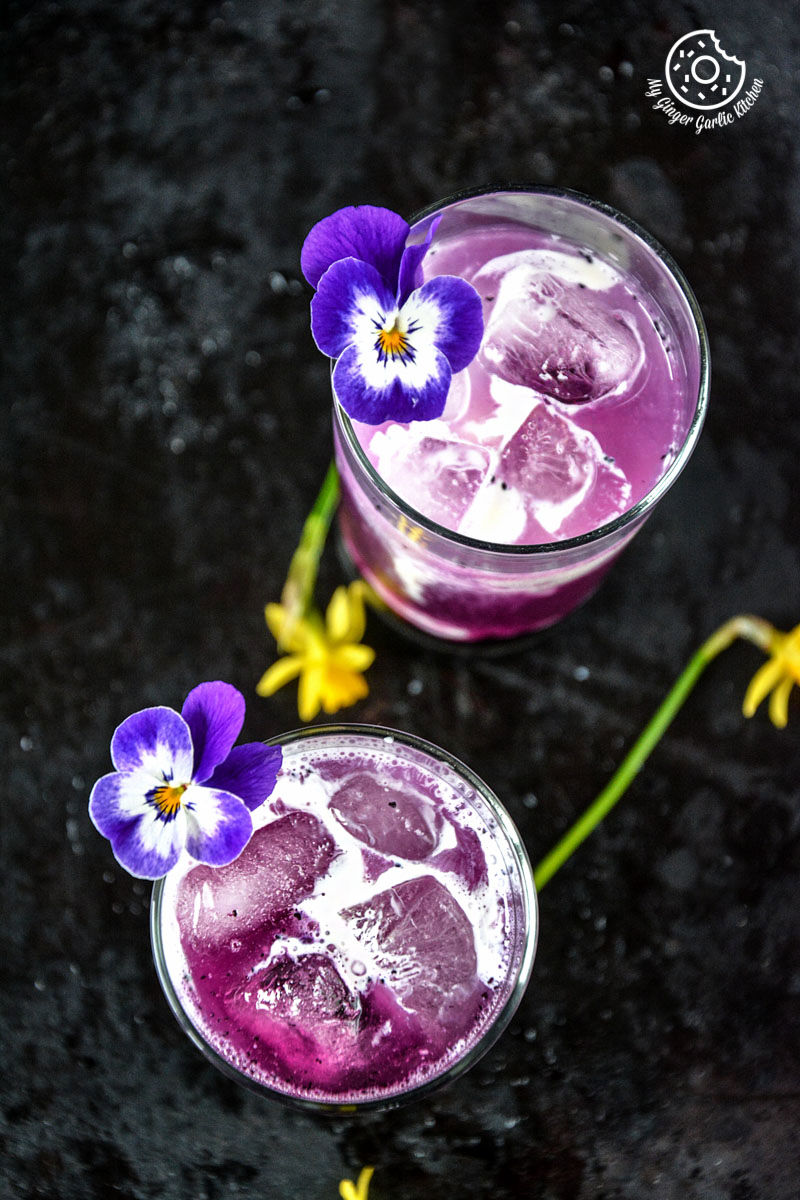 purple drink italian cream soda with ice and flowers on a black surface