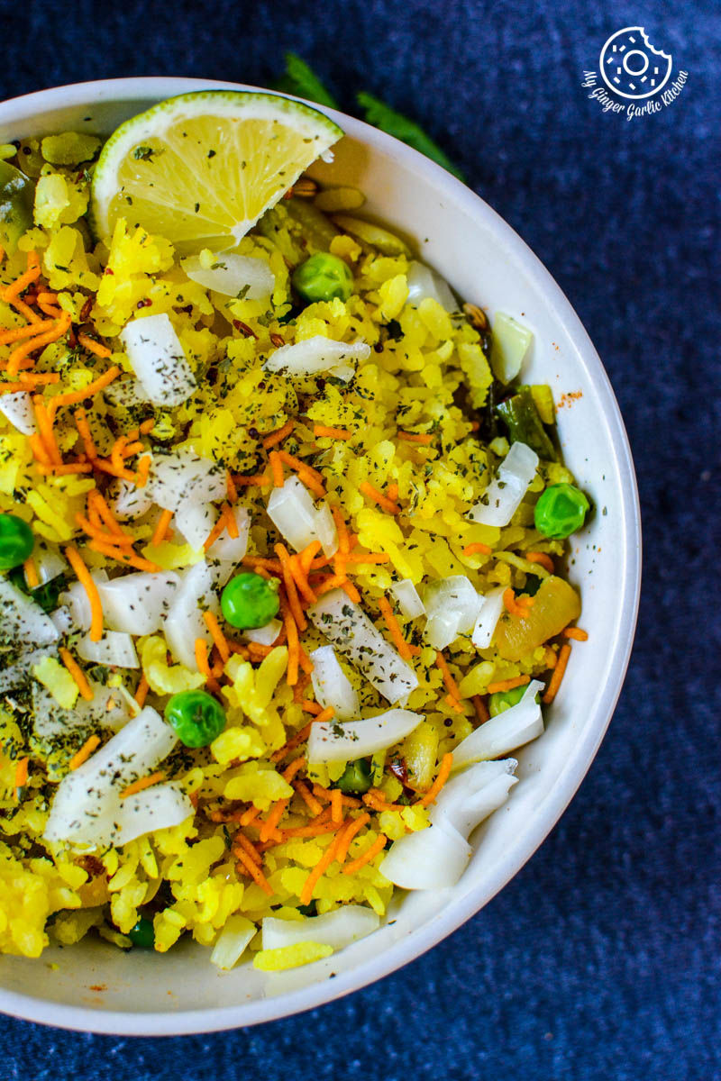 a bowl of khatta meetha indori poha with a topping of sev and cilantro and a lime wedge