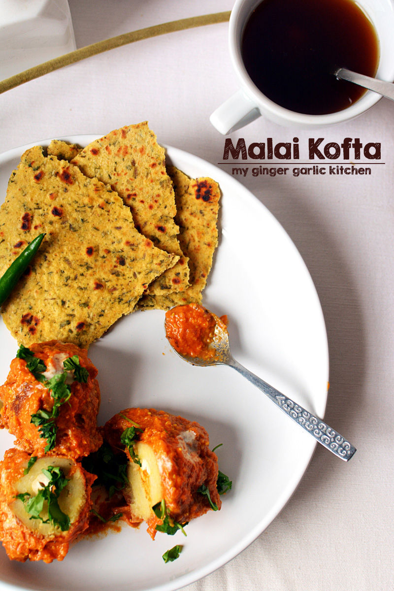 a plate of malai kofta dhana style with a spoon some paratha and a cup of coffee